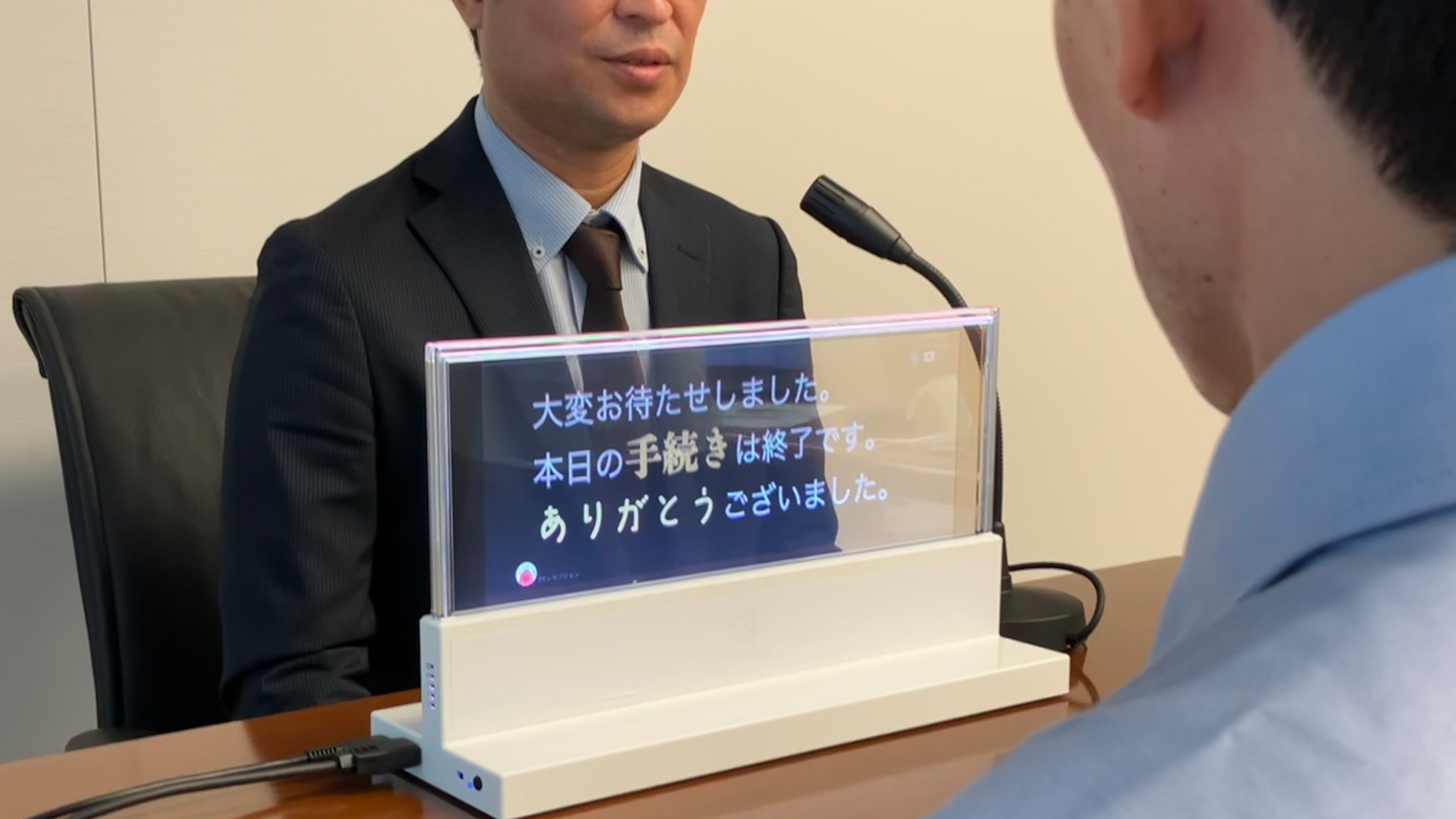 窓口のスタッフの前に「DNP対話支援システム」があり、話した内容が表示されている。